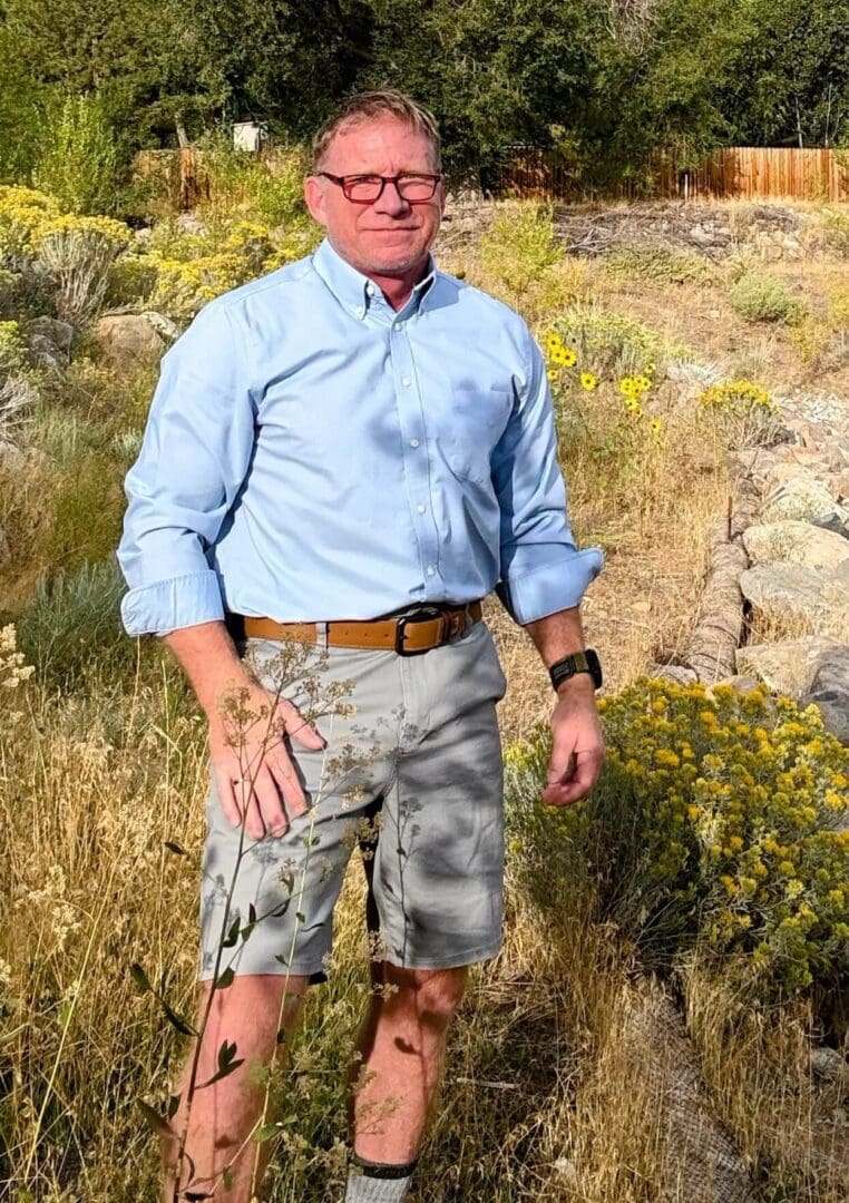 Man wearing a light blue shirt and camouflage shorts outdoors.