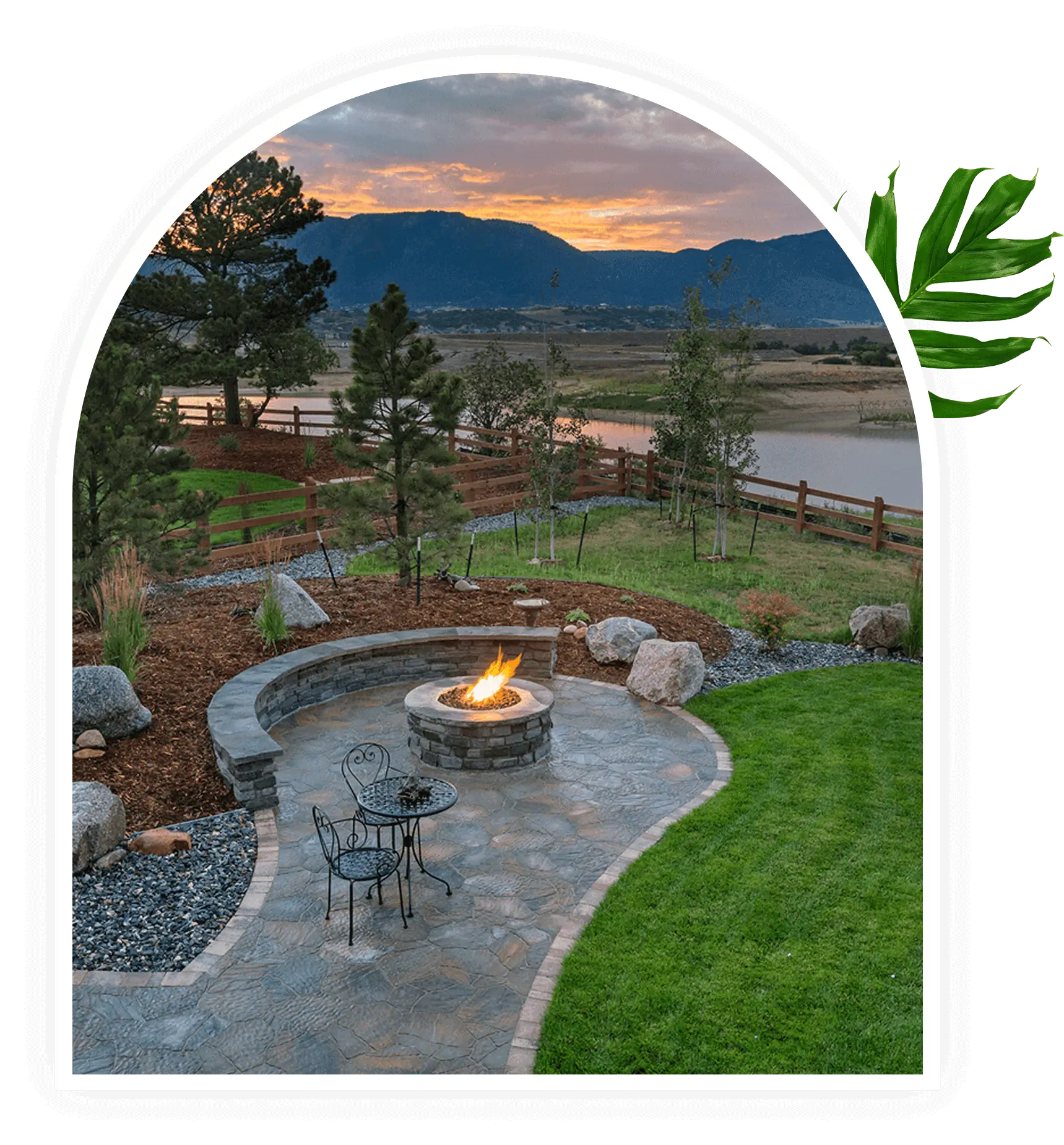 Scenic backyard with a curved stone patio and fire pit at sunset.